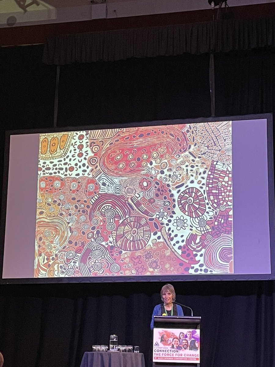 NTShelterInc's tweet photo. Sarah Brown talking about the history of Purple House and showing off some great art at the #NTCOSSConference. She talks about the importance of having people at home, on country during dialysis. “Our patients have the best survival rates on dialysis in the country.” @NTCOSS https://t.co/RwBVxZlxpd