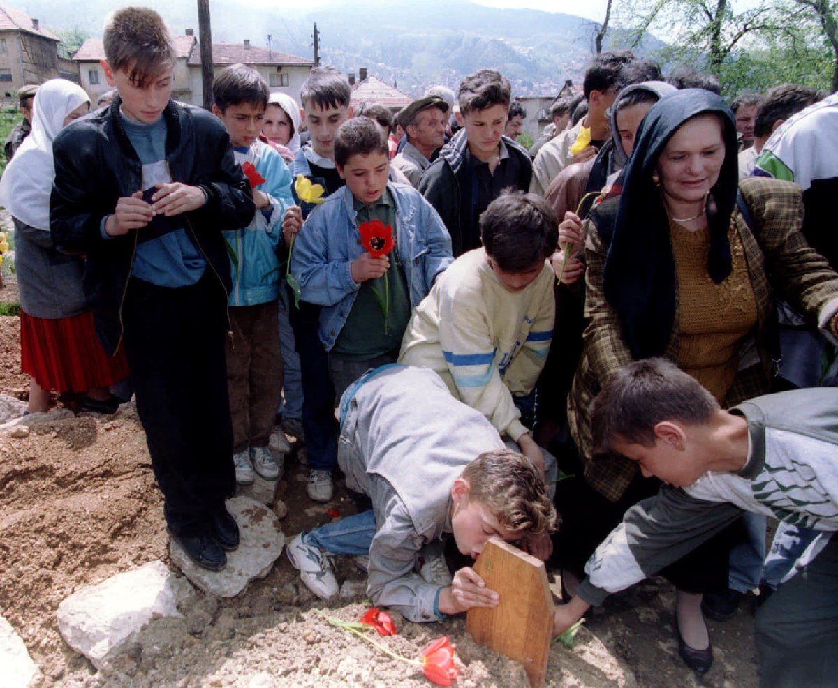 This is the photo from my brother’s funeral from 6 May 1995. My friend Admir kissing Amel’s tombstone and me in the bottom right corner putting down flowers on his grave. When Amel was killed he was only 16 years old. #SarajevoSiege Photo©️Chris Helgren