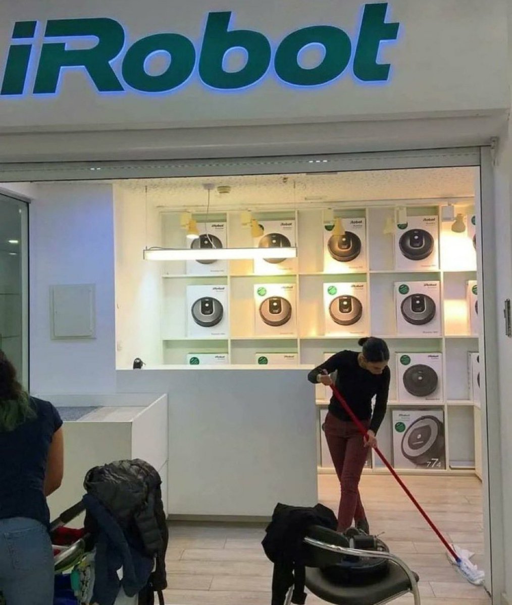 Roomba sitting in a chair watching a human sweep the floors in a Roomba store. It's happening