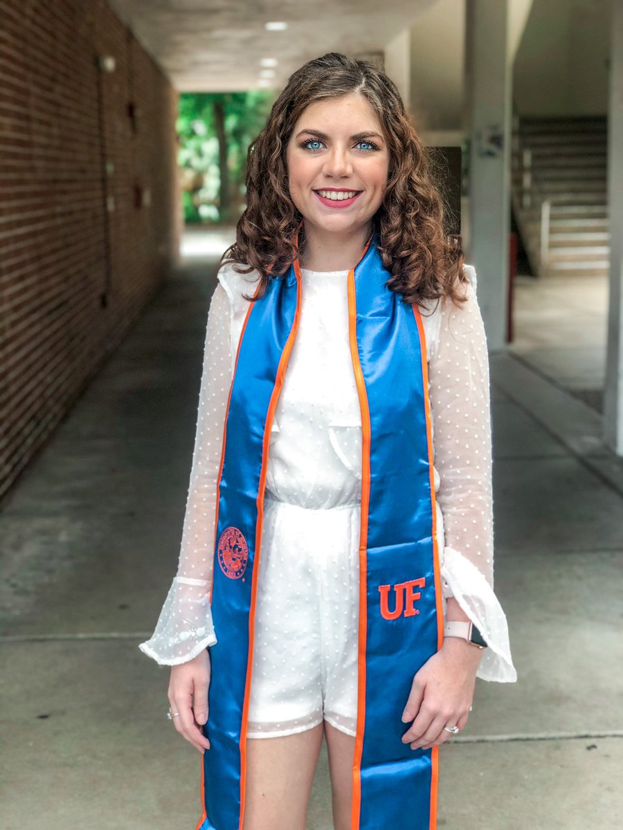 The author is smiling, and you can see a university building in the background. The author is wearing a UF graduation stole around her neck.