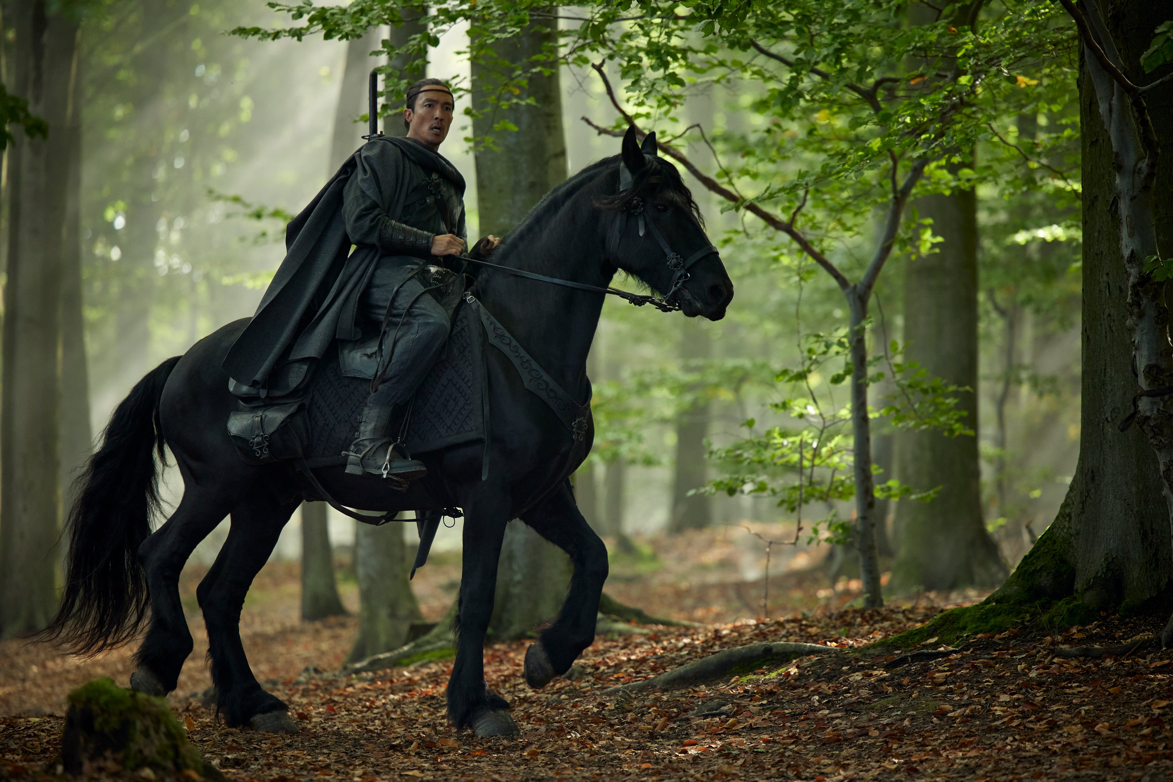 Full shot of Lan, riding a horse through the woods.