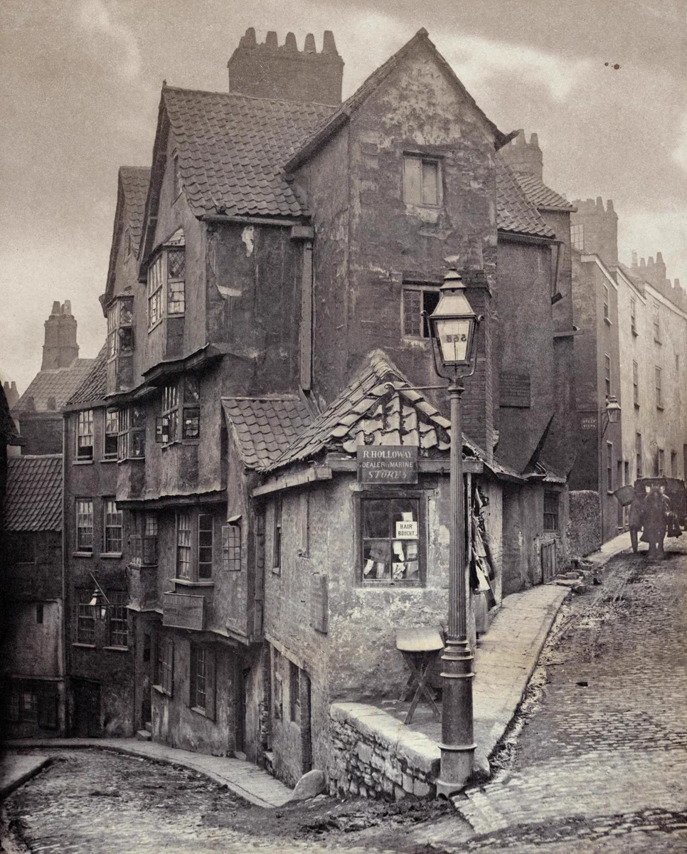 A photograph from 1866 showing the corner between two streets. A shop window has a sign that reads 'hair bought' and an oil lamp is in the front centre of the image. 