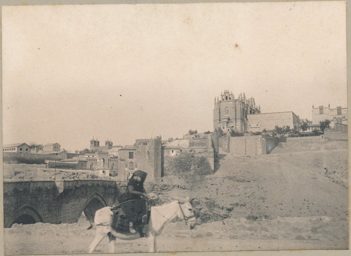 Hace poco incorporé a mi colección personal esta foto de una mujer tapada completamente subida en un burro junto al Puente de San Martín hacia 1900. Se ve al fondo el monasterio de San Juan de los Reyes y también la desaparecida Puerta de San Martín. #Toledo #Castilla