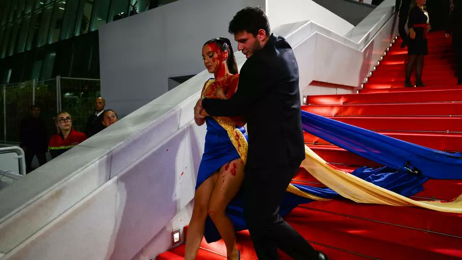 United24media's tweet photo. At Cannes Film Festival, a woman—wearing a dress in the colours of the Ukrainian flag—doused herself in fake blood in protest of Russia's invasion of Ukraine. She did it on the red carpet right before the screening of a Russian film called "Acid". https://t.co/cGDCnMgzit