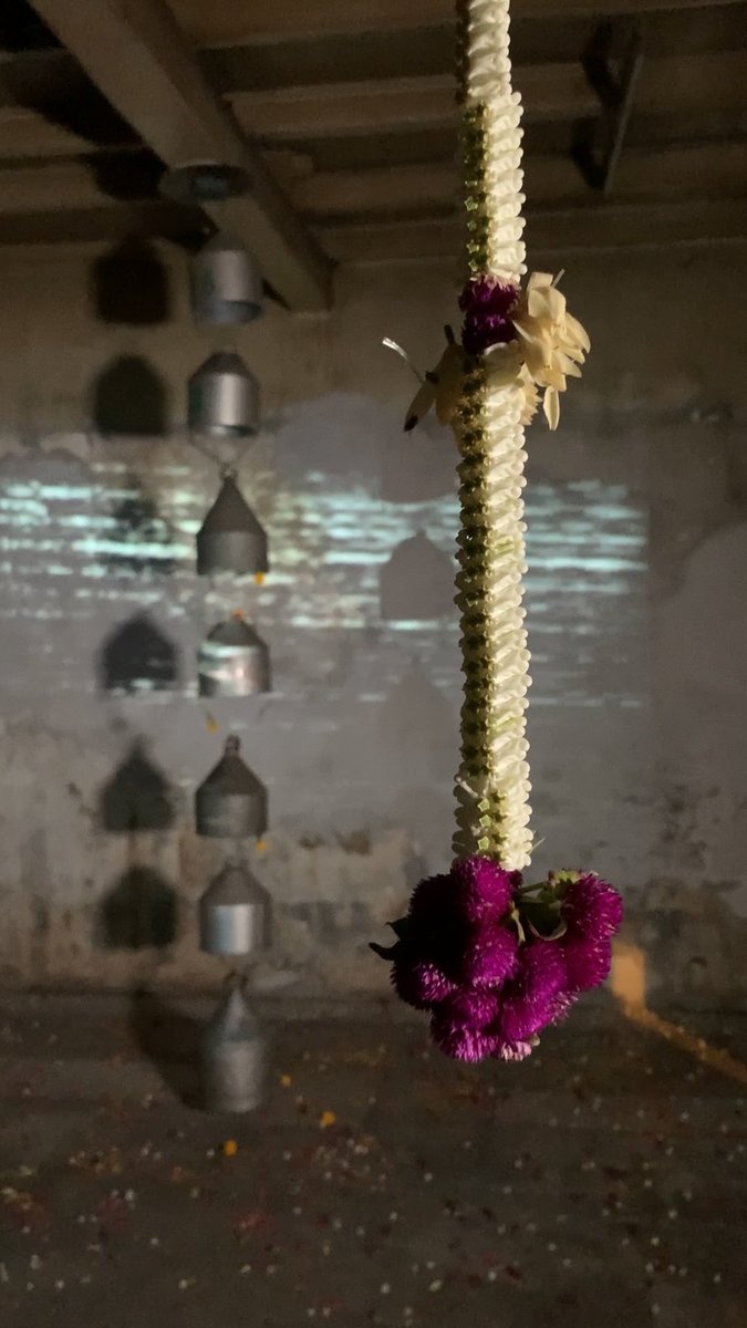 The first room from "The River Cannot Contain the Graces of Dance"  displayed containers for Thai Chatri performers headwear suspended from the ceiling with a visualisation of the film soundtrack as an audio wave, moving like a river of sound. Thai flowers hung nearby. #mediaart