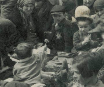 A heart-breaking moment saved in an SS picture of deportations of Hungarian Jews at Auschwitz II-Birkenau. It was taken 79 years ago, most likely in late May 1944. A little child found a dandelion in the grass and is handing it or showing it to an older boy. All the people in