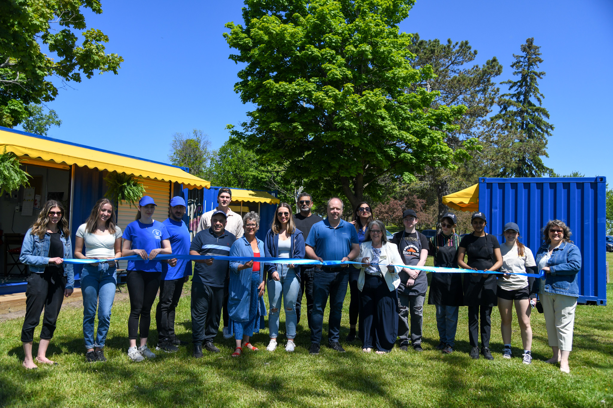 Pop-Ups on the Bay organizers and vendors posing together in front of colourful shipping container booths at the Belleville waterfront festival
