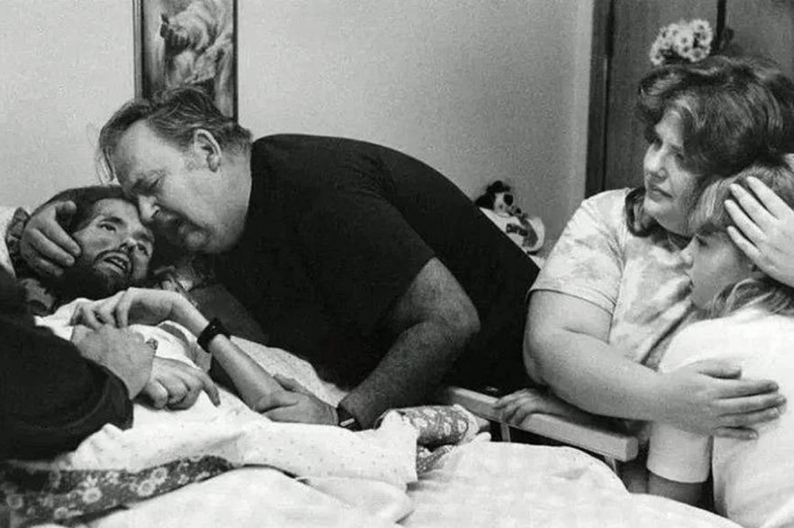 In 1990, David Kirby, a homosexual man who contracted AIDS during the late 1980s epidemic, is captured in this photograph as he lays dying in a hospice center with his family by his side. Although the image portrays his family providing comfort, in reality, they had rejected him…