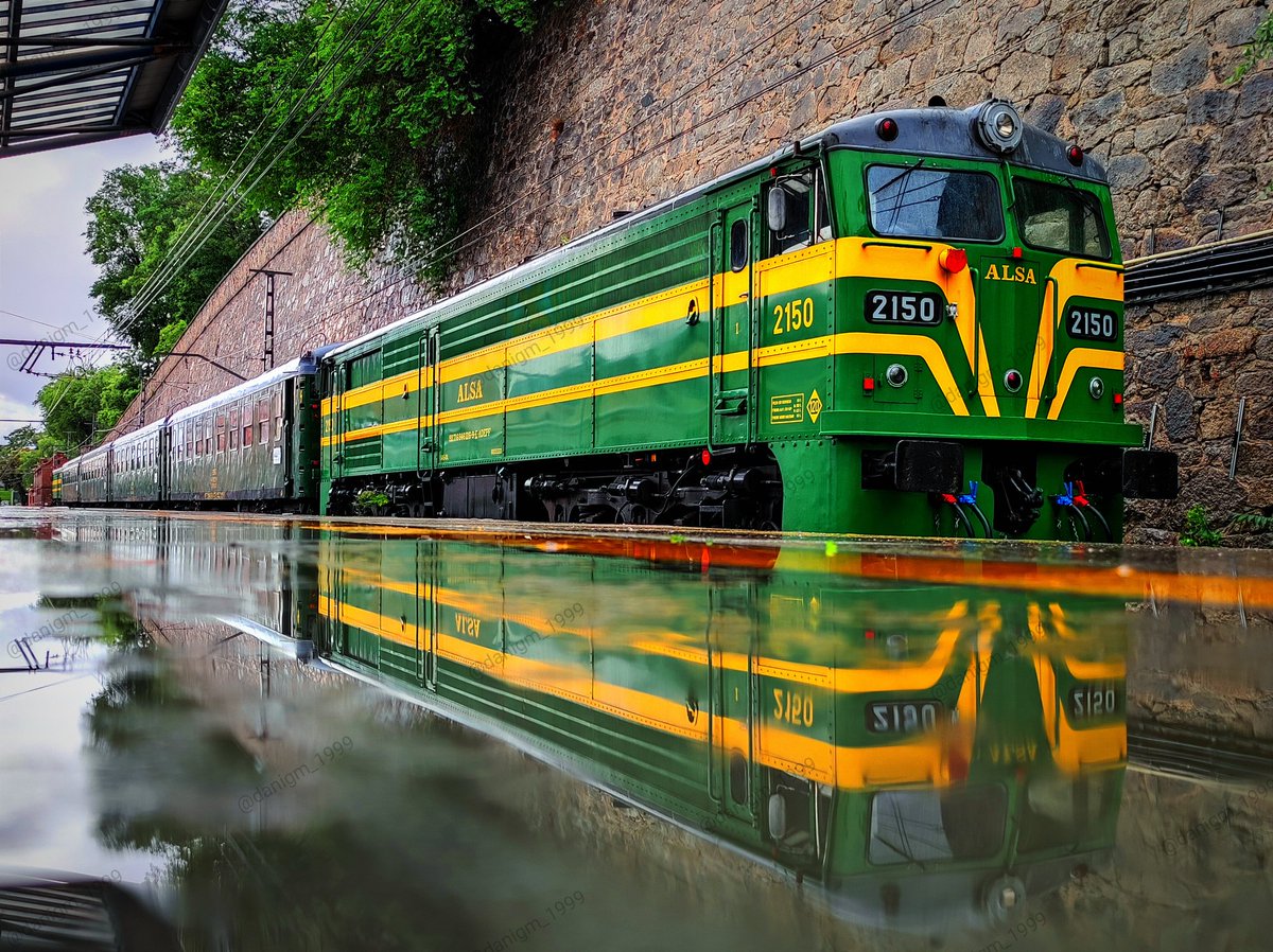 La imponente 2150 de <a href="/Alsa_autobuses/">Alsa</a> y el reflejo nostálgico del <a href="/TrenDeFelipeII/">Tren de Felipe II</a> convergiendo de un suelo lluvioso. ¡Buenos días! 🚂👑