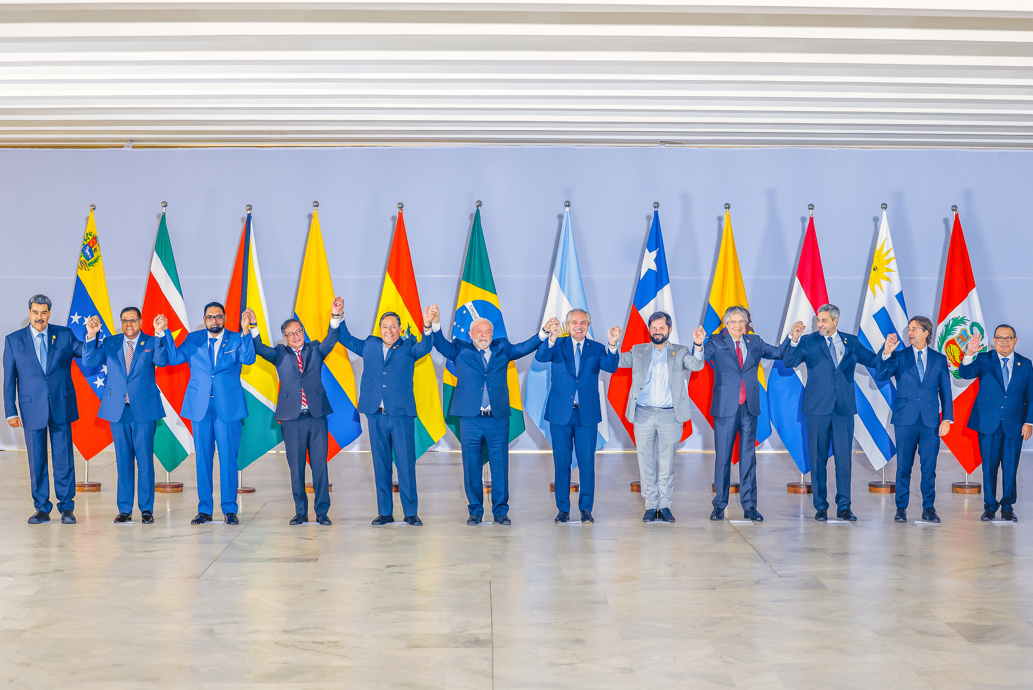 Presidentes da América do Sul erguem as mãos unidades, em frente as bandeiras dos seus países