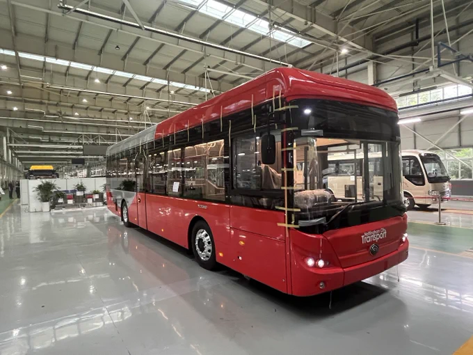 Offside view (roadside) of the first NCT battery electric bus in the factory in China. The bus is red and silver.