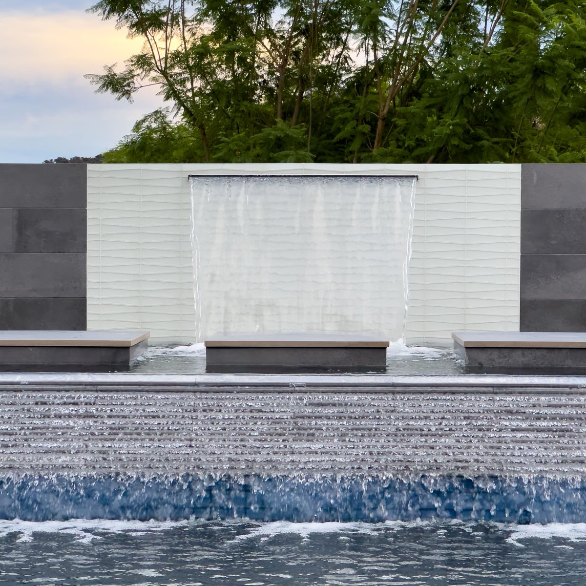 Upgrade your pool design with a waterfall feature! Not only does it create a serene and relaxing ambiance, but the sound of the cascading water is soothing to the mind and body. 🌊💦 #pooldesign #waterfallfeature #relaxation