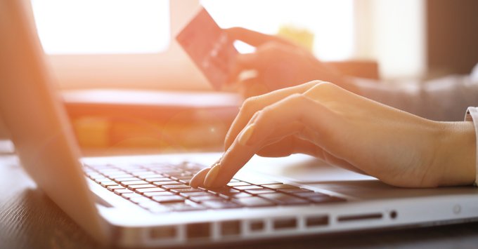 A hand is hovering over a computer keyboard. The other hand is holding a credit card. 