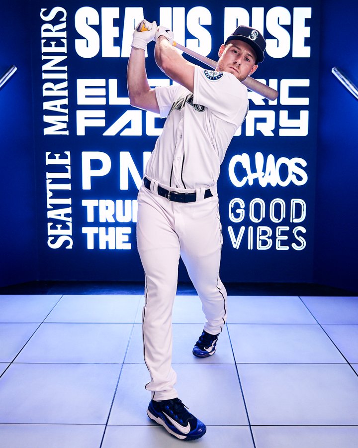 Photo of Jarred Kelenic swinging a baseball bat while wearing the classic home white uniform. 
