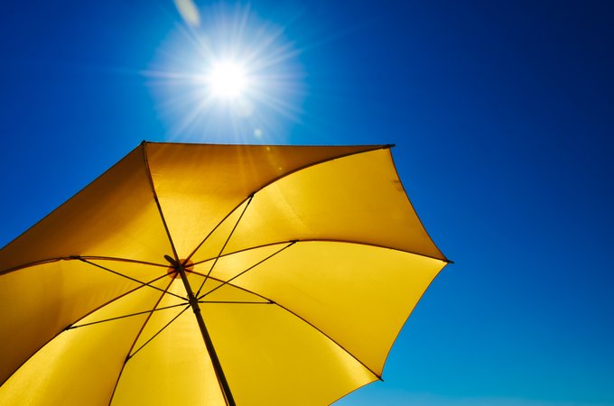 An image of a yellow umbrella next to a very bright sun in a cloudless blue sky.
