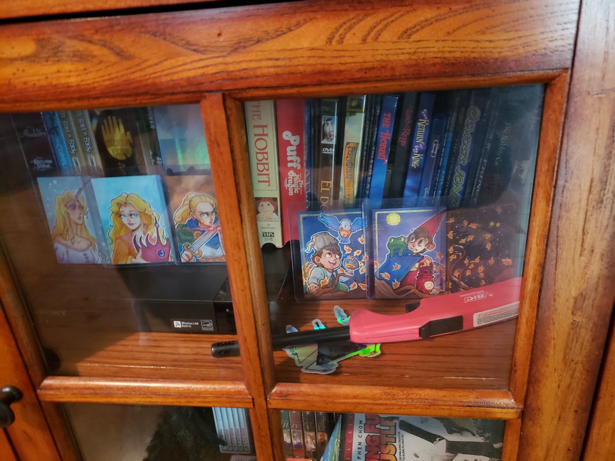 Close-up of our entertainment cabinet, which includes @Yamcans sketchcards of Rankin-Bass fantasy leading ladies and an 'Over The Garden Wall' triptych set.