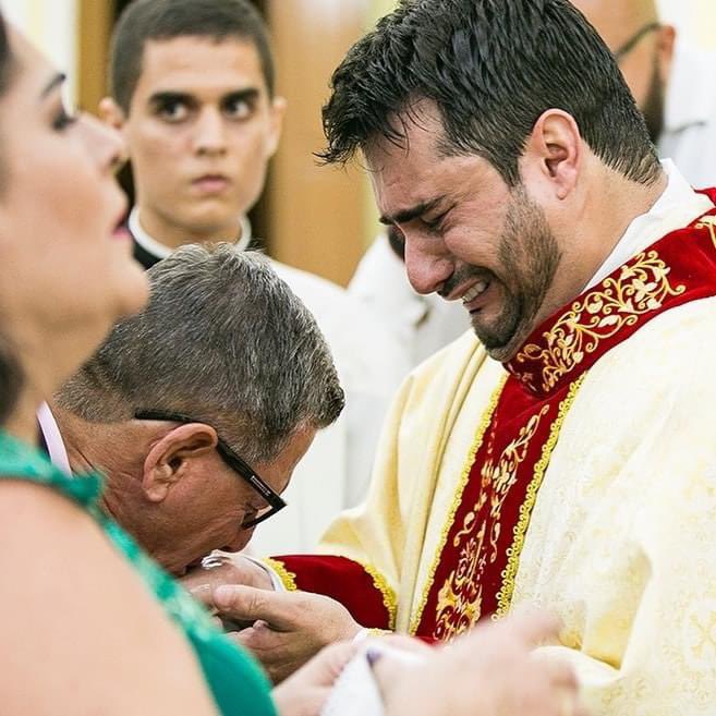 Father of a newly ordained Catholic priest kisses the anointed hands of his son.