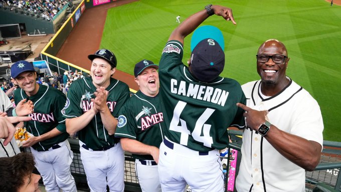 A group of fans dressed as the 2001 Mariners meet Mariners legend Mike Cameron, who is pointing at the back of the jersey of the fan dressed as Cameron. 