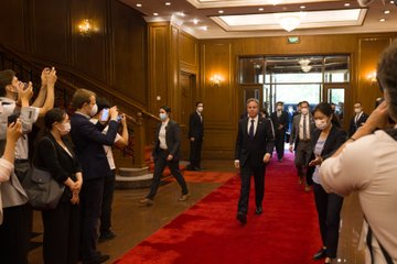 Secretary Blinken walks down a hallway. People stand at the sides and take photos. 