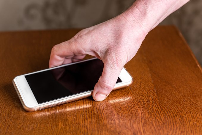 Une main ramasse un téléphone portable sur une table.