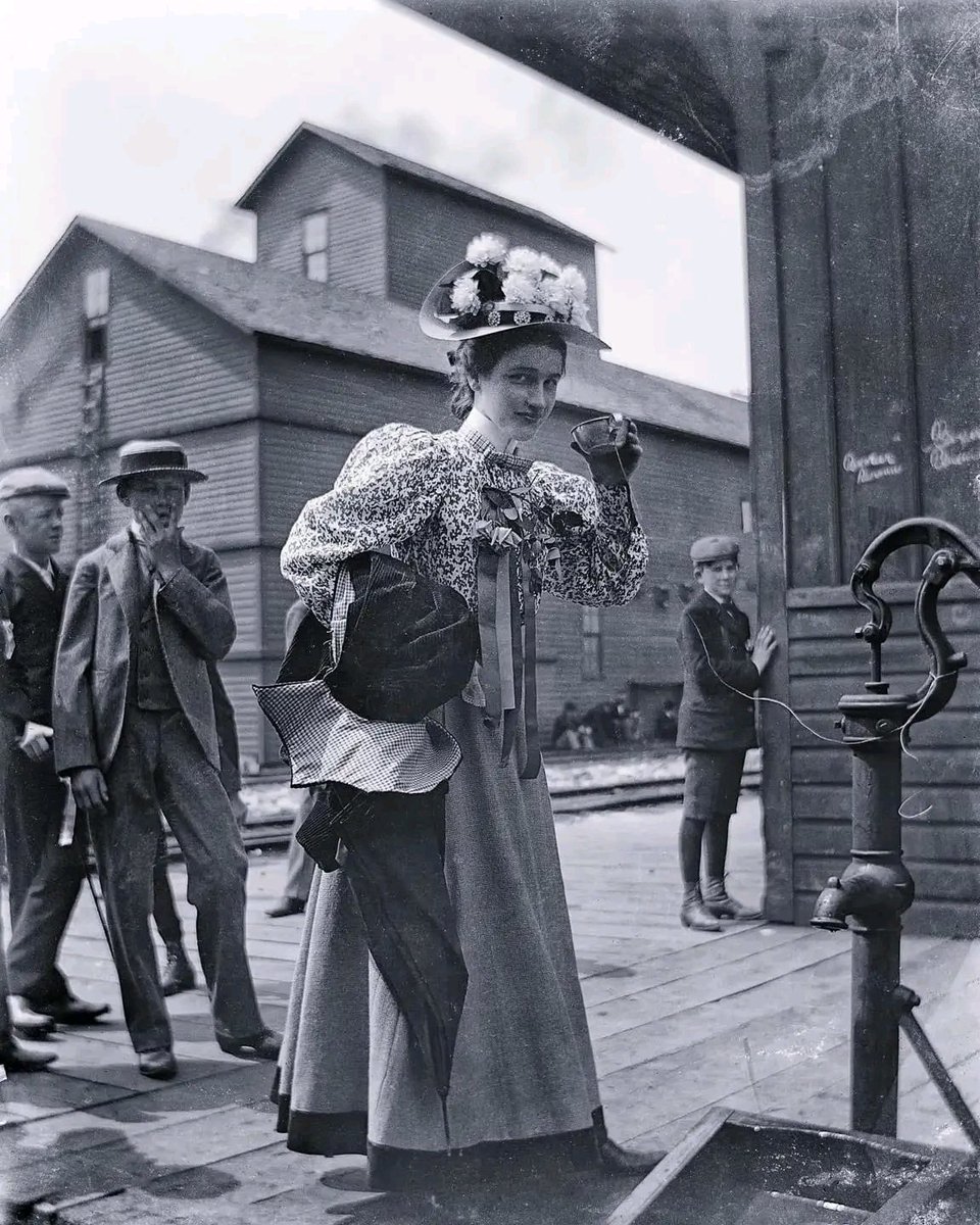 A woman drinking from a common cup attached to a water pump, Chicago, 1899. That rude boy in the back!