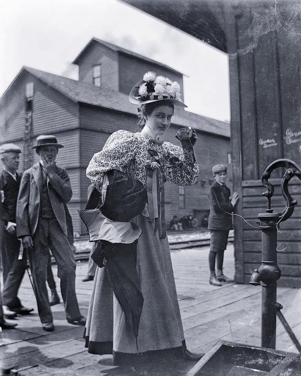 ☂️🎶Happy Friday 🎶☂️ here’s a beautifully stylish woman drinking from a common cup attached to a water pump, Chicago, 1899. 🌺 📷 notice the boy photobombing 🤣🎶everything old is new again🎶📸🎶🎭🐸🎩☂️📸🎷🎶🎹💚☂️