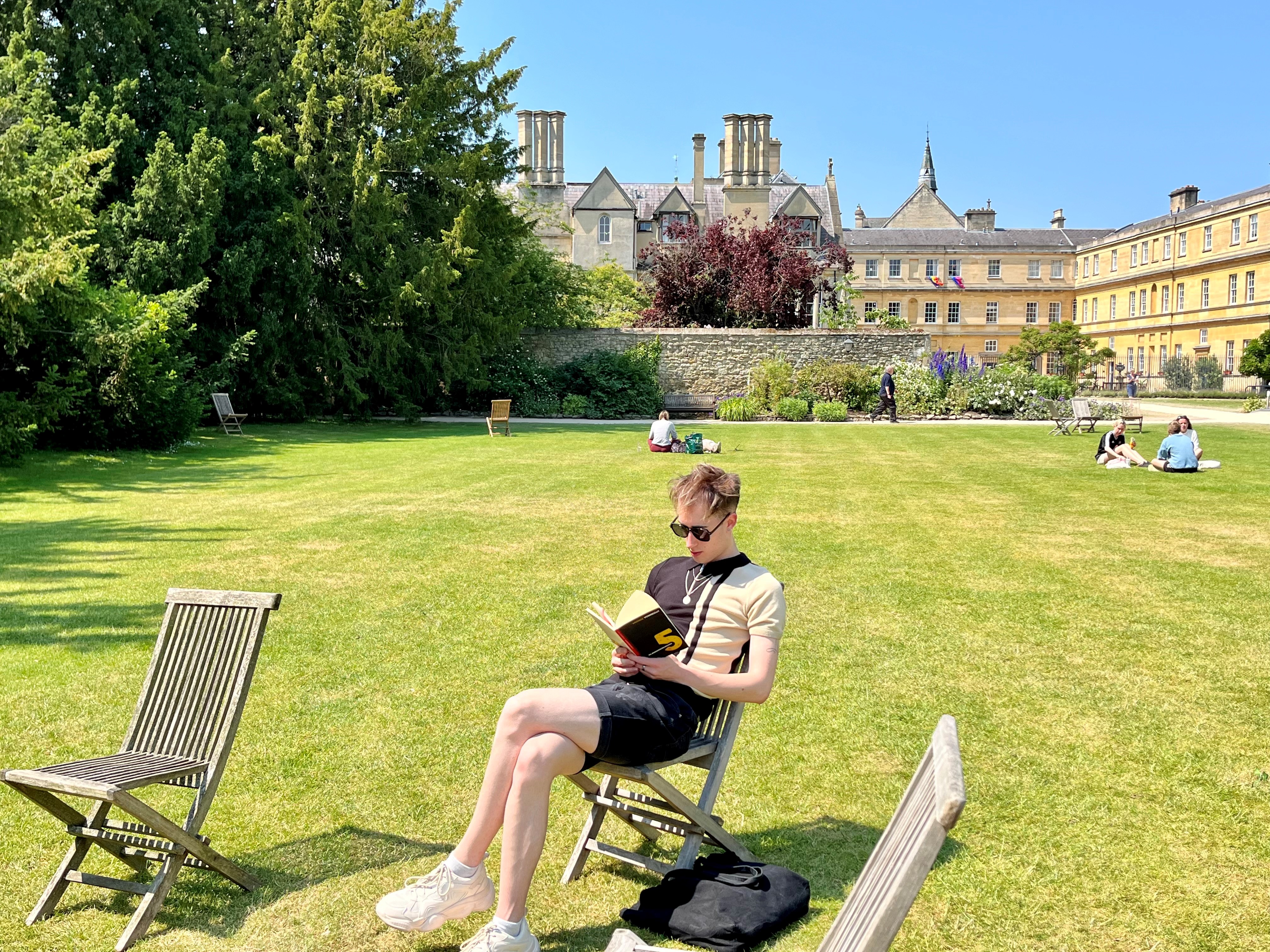 A student sits reading in a garden chair on the lawns at Trinity.