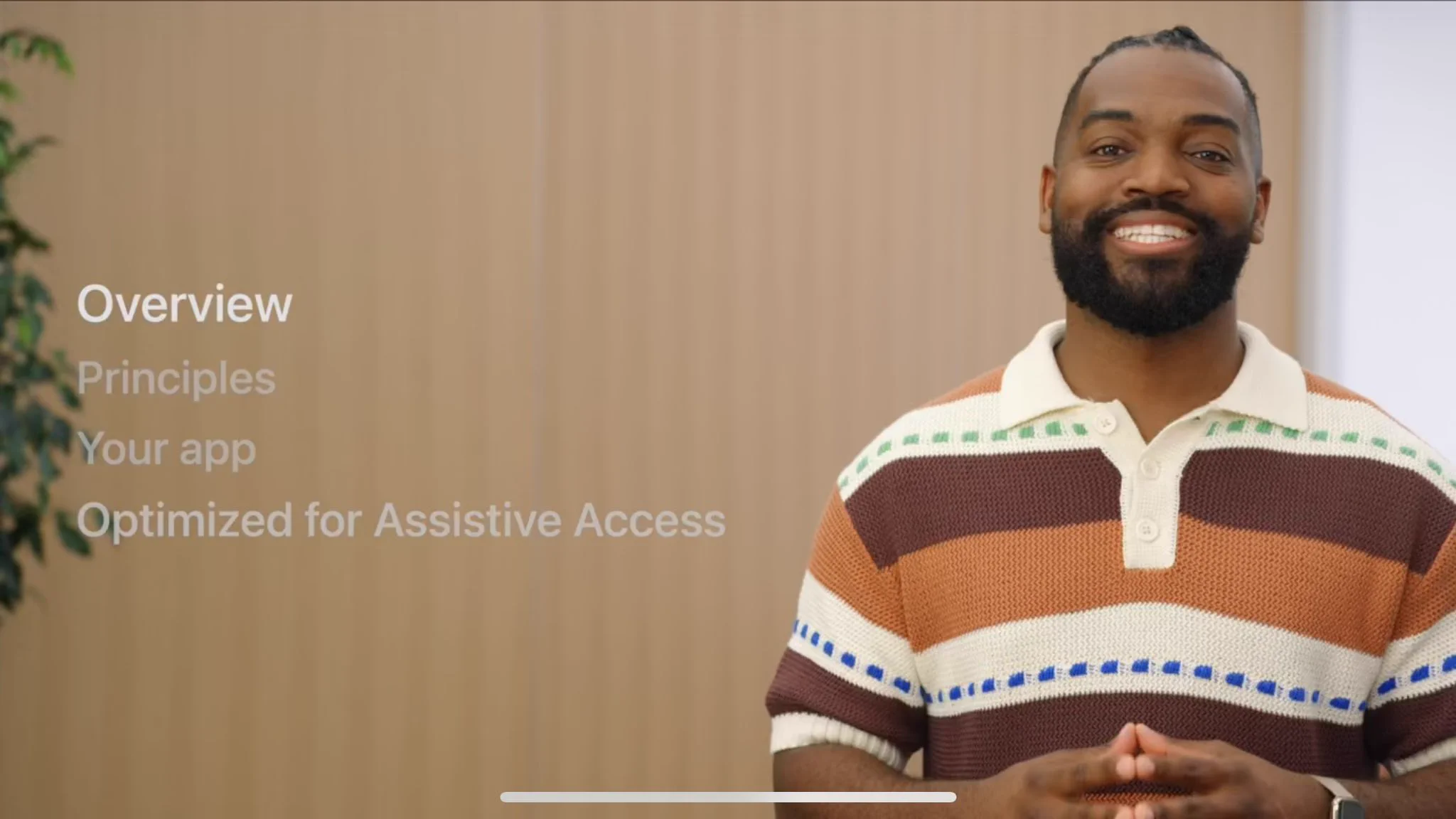 Screenshot from my WWDC session “Meet Assistive Access”. I’m smiling and wearing a horizontal striped shirt with cream, dark and light brown stripes. Also in view shown is an outline of the presentation as with the sections: Overview, Principles, Your App, & Optimized for Assistive Access.