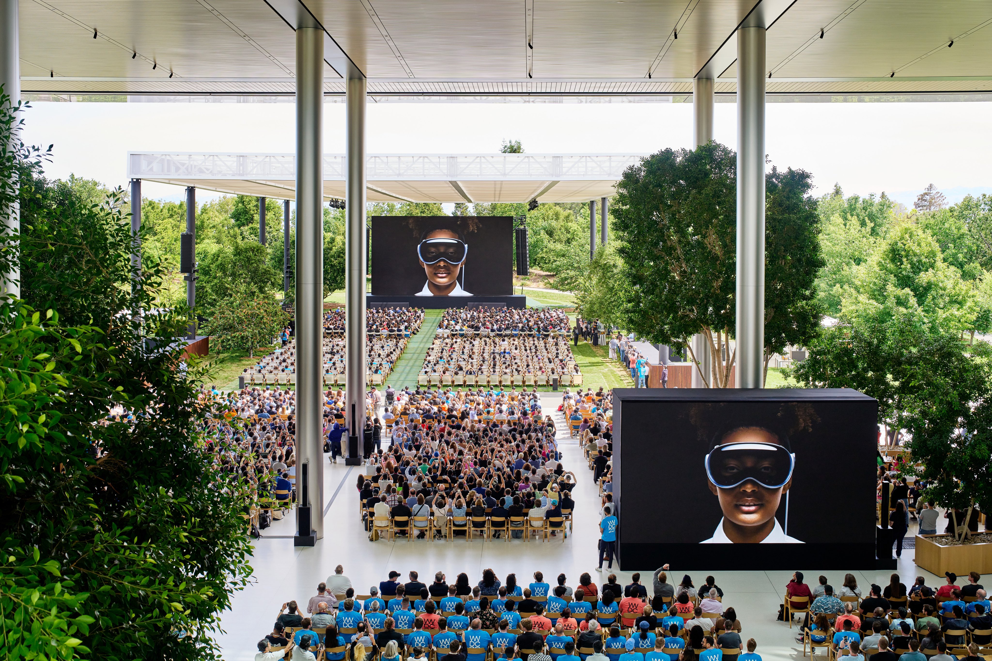 Hundreds of people sit in chairs at Apple Park watching the WWDC keynote.