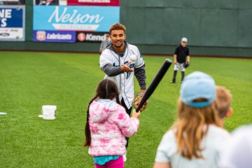 Photo of Mariners prospect and Everett AquaSox catcher, Harry Ford, tossing a baseball to a young fan during our Play Ball Weekend event. 