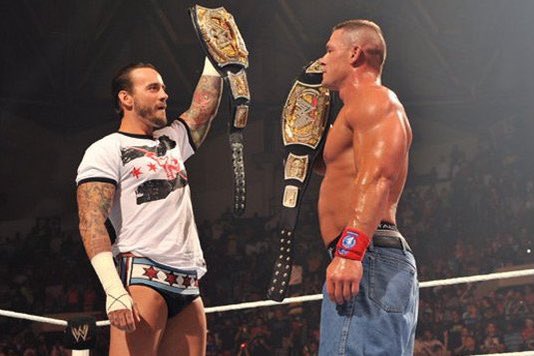 John Cena first raises his fake WWE title to a mixed reaction then CM Punk raises his real WWE championship to a loud pop while John lowers his arm down.