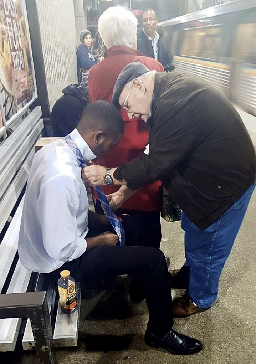 “This young man was on his way to a job interview and had a bit of trouble with his tie.

The lady in the red coat noticed him struggling and nudged her husband with her elbow. 

She then blocked him to help him evade any embarrassment. 

Her husband not only helped the man with