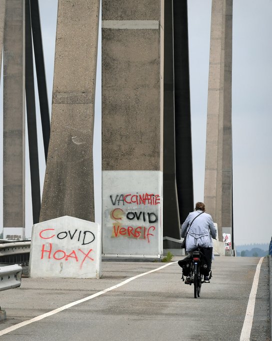 Een voorbijganger op de Prins Willem Alexanderbrug over de Waal fietst langs grafitti leuzen die het coronavirus en de betrouwbaarheid van traditionele nieuwsmedia in twijfel trekken. Foto ANP 