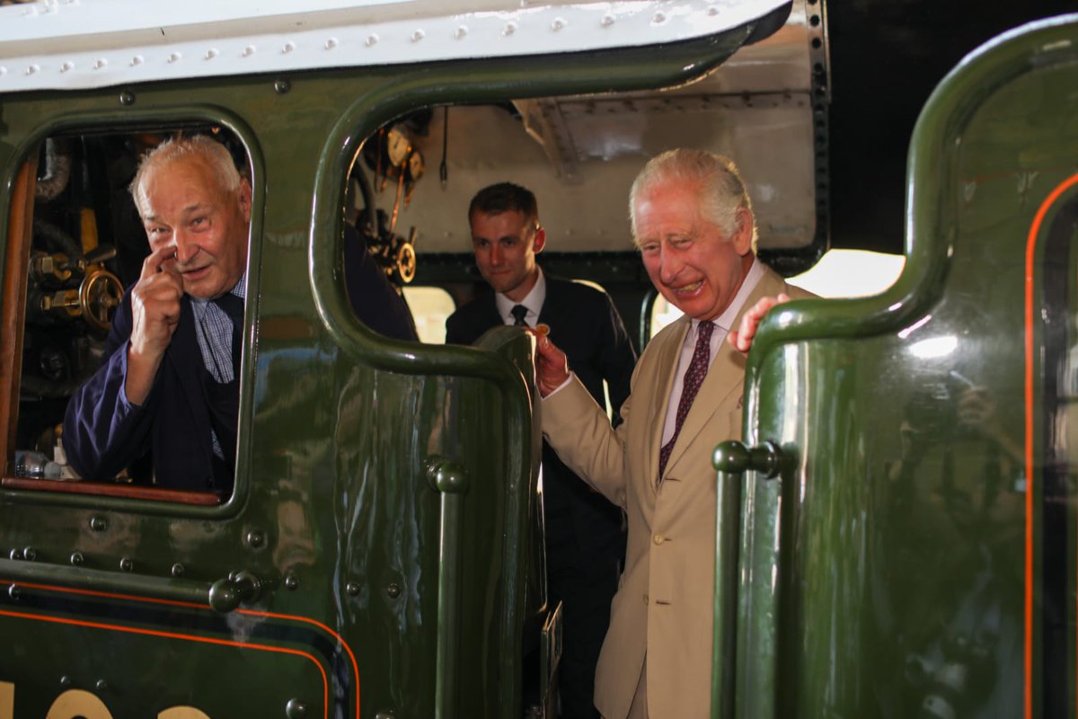 His Majesty The King stands smiling aboard the footplate of Flying Scotsman. Two crew are also on board.