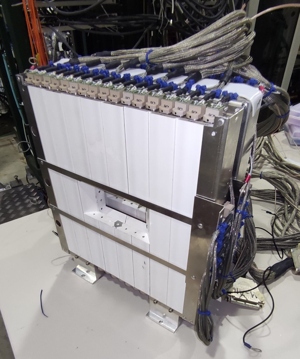 This photo shows one station of the CHANTI detector. The white part is a stack of triangular-shaped plastic scintillator, which produce light when a charged particle passes through them. The light is collected by silicon photo-multipliers located at each end of the bar.