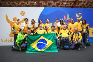 Foto das seleções brasileiras de vôlei sentado mostrando a bandeira do Brasil com suas medalhas de ouro no peito.