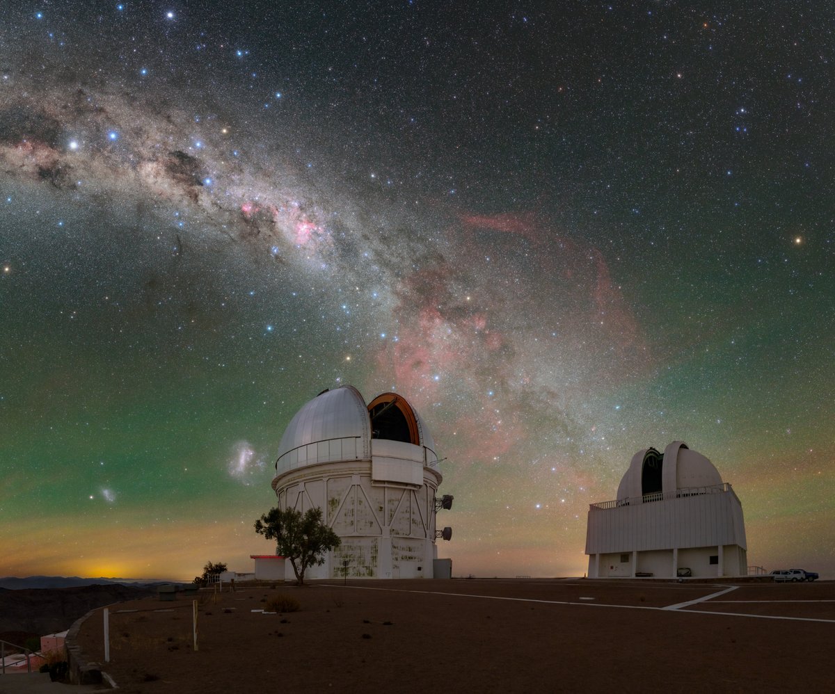 Speckled with multi-colored stars, our home galaxy in this image stretches down into the city-lit horizon, just grazing past the Víctor M. Blanco 4-meter Telescope (left) and SMARTS 1.5-meter Telescope (right). The Small and Large Magellanic Clouds that accompany our home galaxy are seen to the left of the Blanco telescope. In between the telescopes blooms a deep shade of red that permeates through the tendrils of the Milky Way. This is the Gum Nebula, an emission nebula that blazes with the light of gas ionized by its host stars.