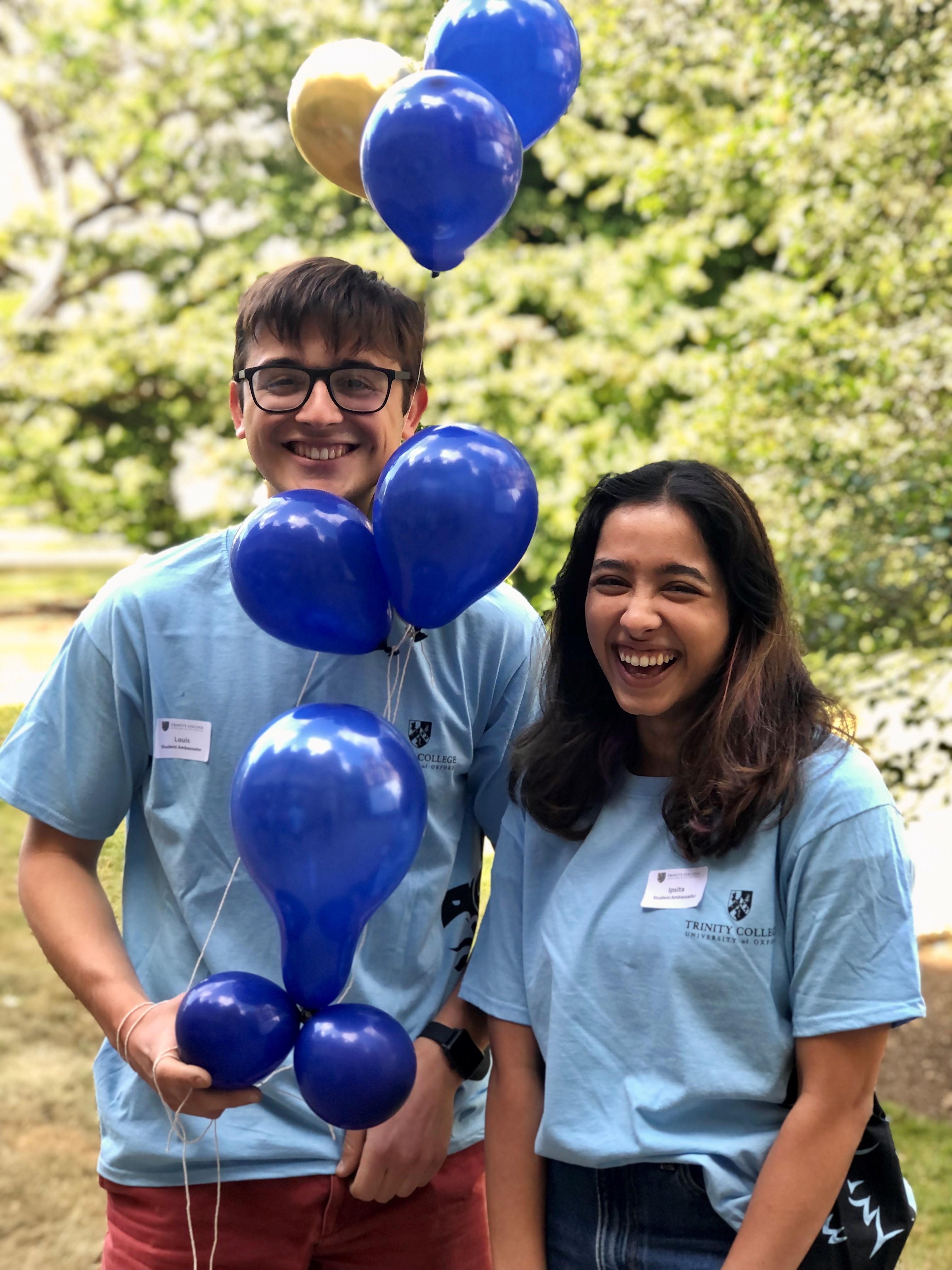 Two Trinity student ambassadors stand holding balloons for open days.