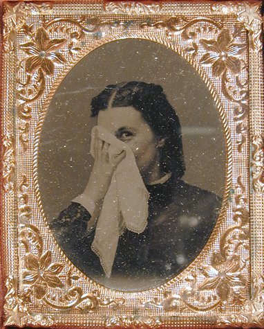 'Tintype portrait of a woman smiling coyly from behind a handkerchief'. Photographed in the 1860s. San Francisco Museum of Modern Art, Photography Collections.