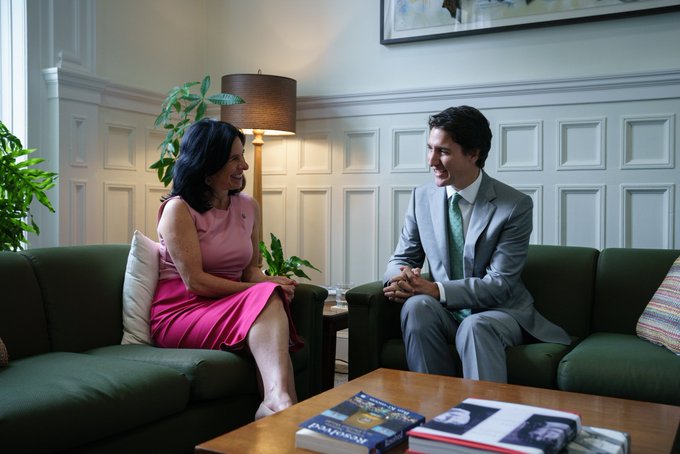 Le premier ministre Justin Trudeau et la mairesse Valérie Plante sont assis sur des divans l'un à côté de l'autre. Ils se regardent et sourient. Derrière eux, on peut voir des plantes et une lampe. Devant eux, on peut voir une table basse sur laquelle sont posés des livres.