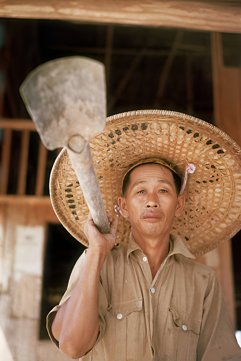 Tin miner from Malayasia wearing broad hat and carrying shovel in 1953