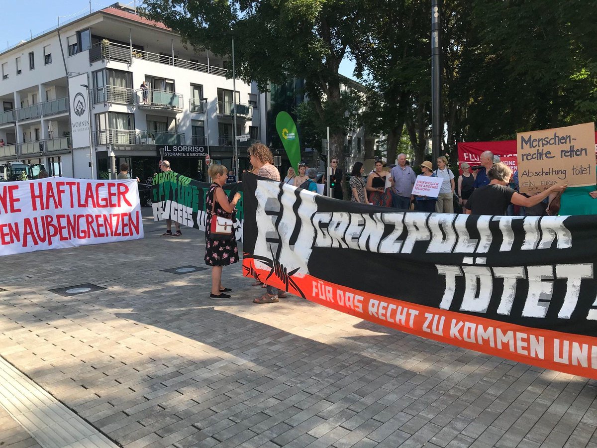 Menschen mit Transpis vor dem Tagungszentrum in Bad Vilbel.<br>'KEINE HAFTLAGER AN DEN AU?ENGRENZEN'<br>'EU GRENZPOLITIK TÖTET'<br>'Menschenrechte retten'<br>Im Hintergrund ist eine Grünen-Fahne zu sehen.