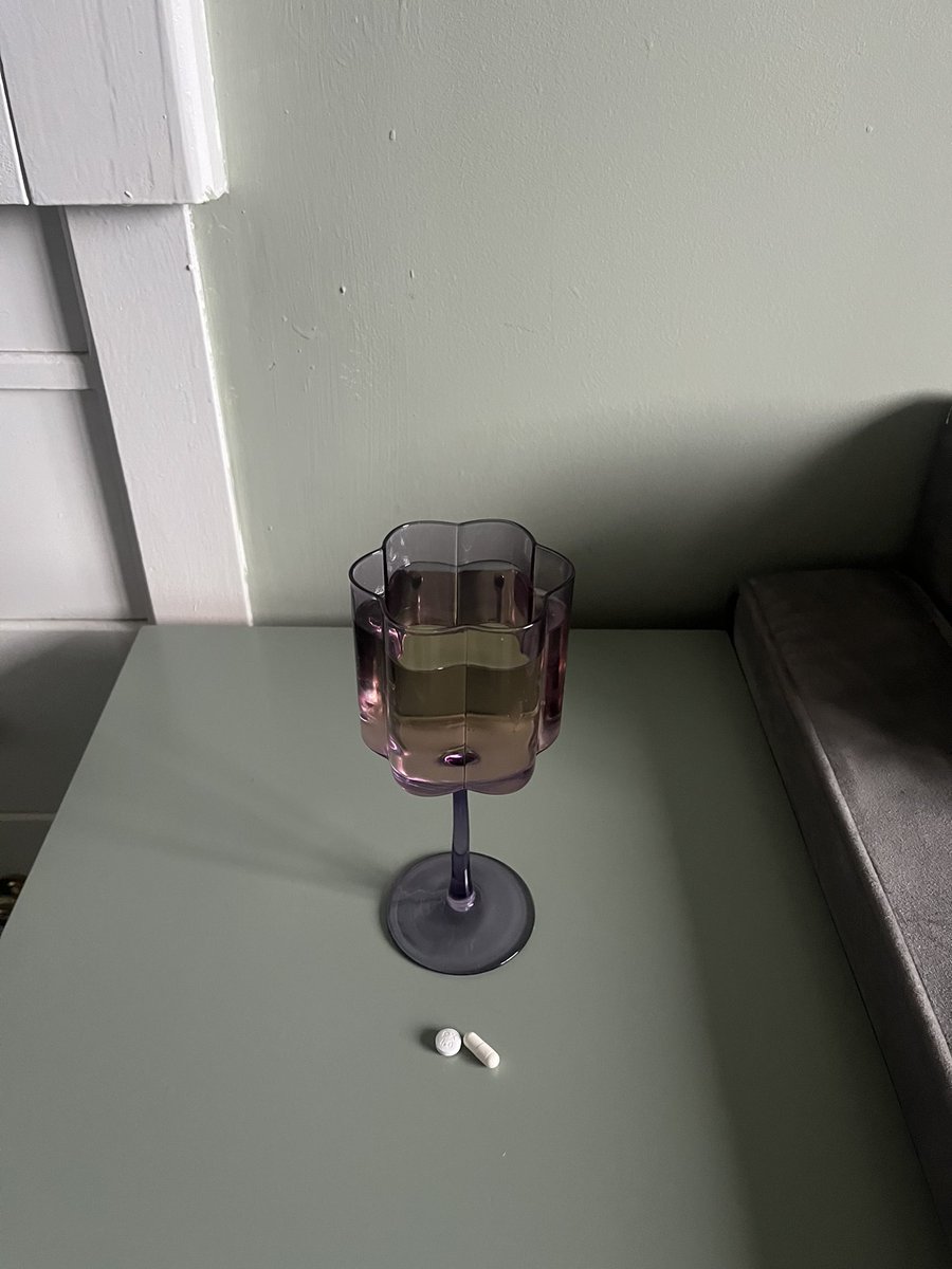 art piece: recently dumped woman edging in on 30 captures purple flower glass of wine she’s about to sip from to take her rheumatoid arthritis medication & anti-depressants. -2023