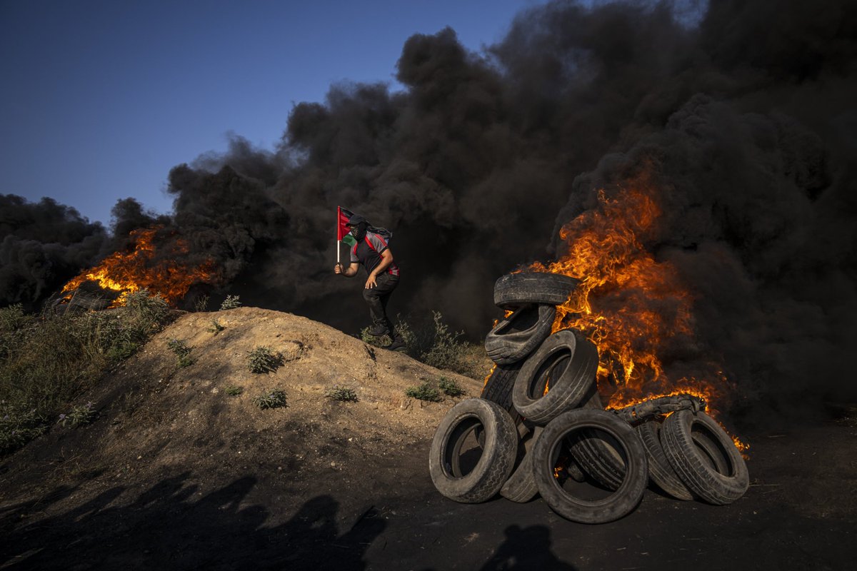 Palestinians burn tires and wave the national flag during a protest against an Israeli military raid in the West Bank city of Jenin, along the border fence with Israel, east of Gaza City, Monday, June 19, 2023. (AP Photo/Fatima Shbair)