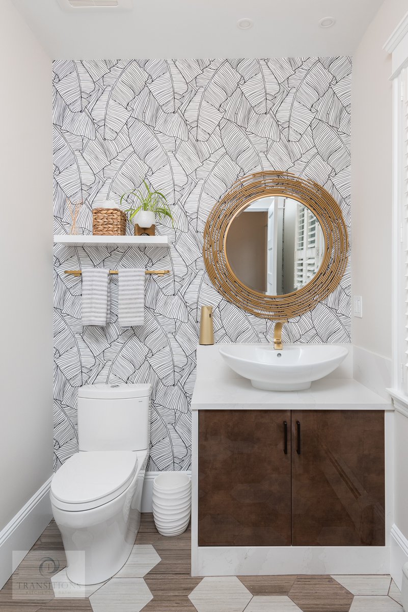 There's so much to love about this glamorous powder room design! From the two-toned hexagonal tile floor to the patterned wall décor, gold accessories, and bold framed mirror, this #bathdesign is a style icon.  
 👉Talk to our team about your #bathremodeling plans!