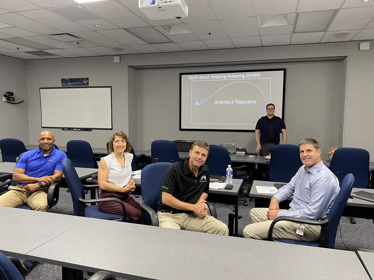 The Artemis II crew in a classroom with a person giving a presentation on Artemis II trajectory. // L’équipage d’Artemis II dans une classe avec une personne donnant une présentation sur la trajectoire de la mission.