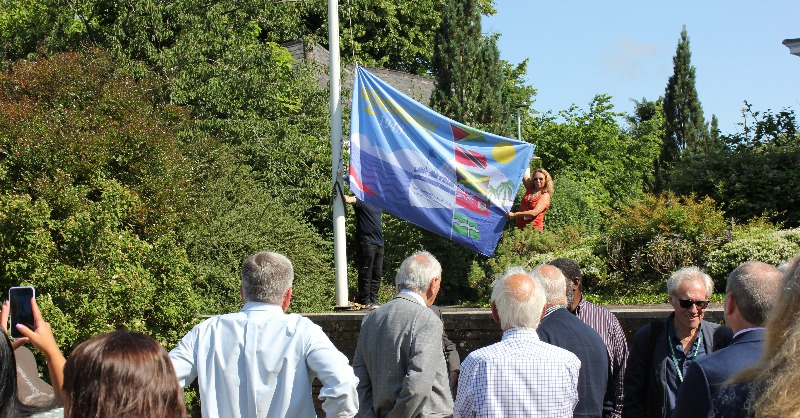 DevonCC's tweet photo. The Devon Windrush Flag was raised at County Hall today to mark 75 years since the Empire Windrush arrived in Tilbury Dock in a symbolic moment for Britain.

#Windrush75 🧡