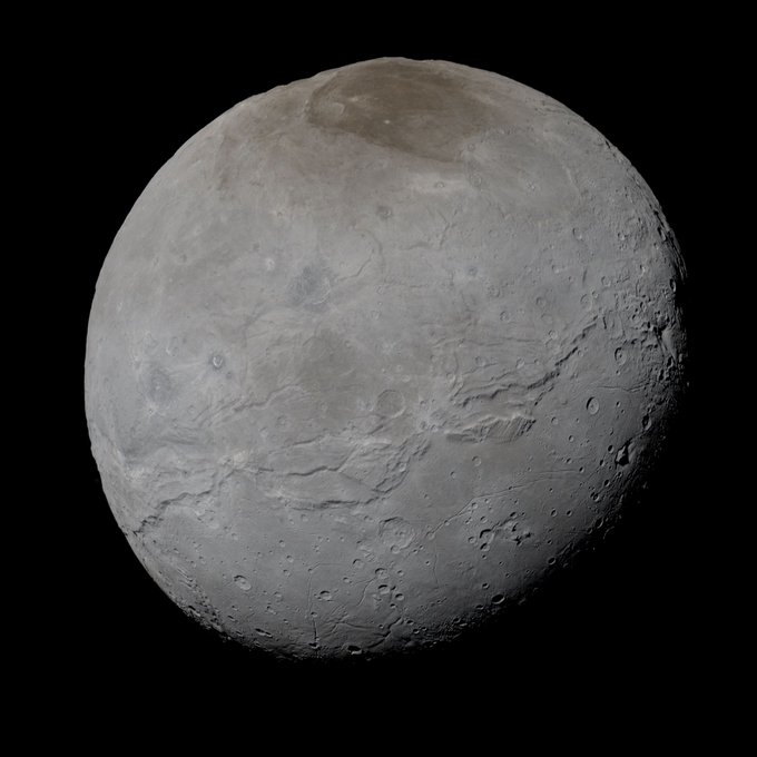 Charon, a grey moon with a large brown-ish spot at the top.