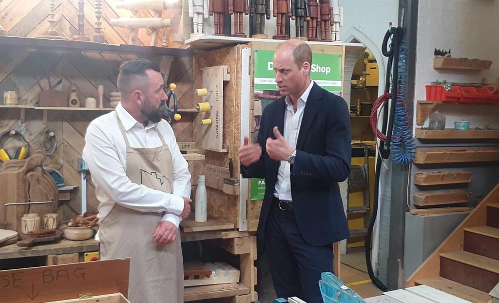 The Prince of Wales has moved into the carpentry workshop where he is speaking with trainer Rob Cox.