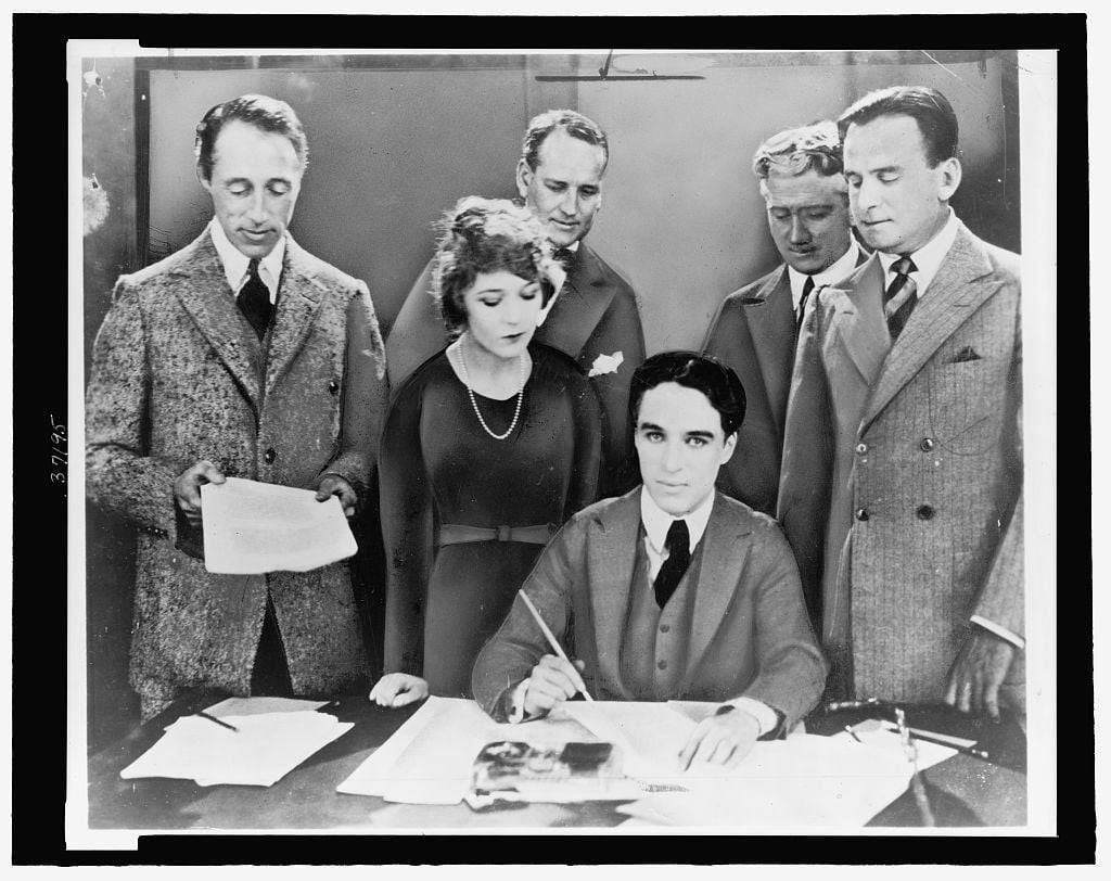 'D.W. Griffith, Mary Pickford, Charlie Chaplin (seated), and Douglas Fairbanks at the signing of the contract establishing United Artists Motion-Picture Studio - 1919.'